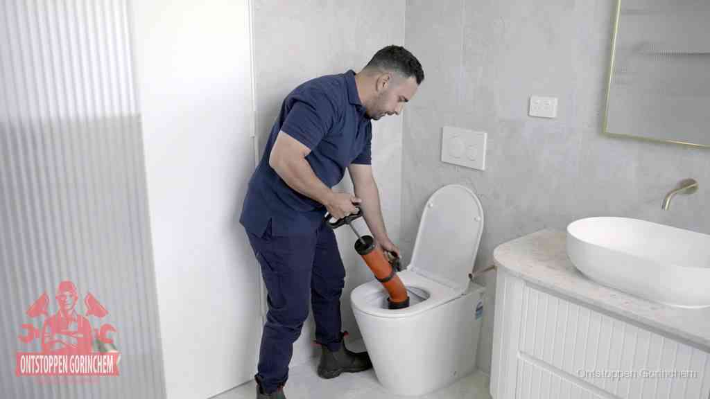 Een monteur buigt over een wandcloset en duwt met de hand een persluchtontstopper in de toiletpot om de verstopping handmatig los te maken in Gorinchem
