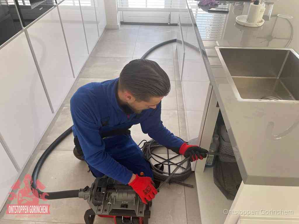 Een monteur ontstopt de keukenafvoer onder de spoelbak met een elektrische veermachine in Gorinchem