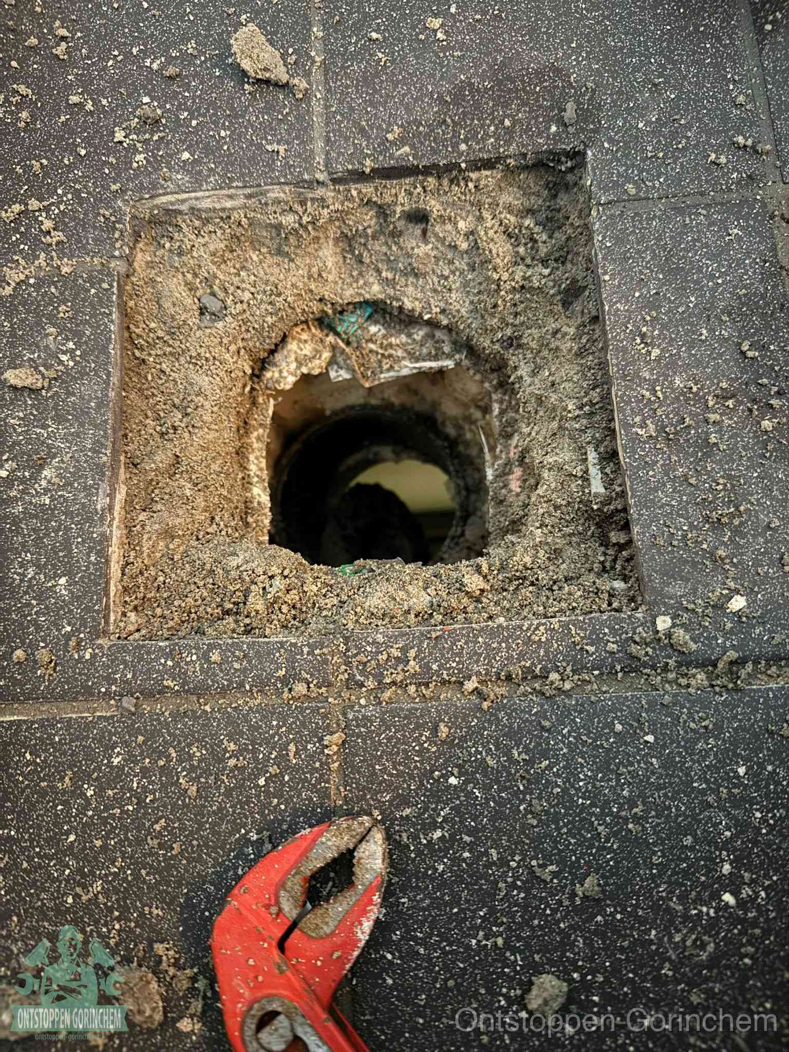 Een geopend rioolputje in een betontegelvloer met losgemaakt rooster en een zichtbare ronde afvoerbuis, het achterhalen waar de afvoerverstopping zit in Gorinchem