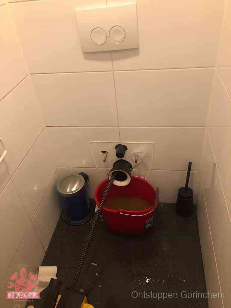 Een ontstopte wand-wc met verwijderde toiletpot waar een ontstoppingsveer in de wanduitgang verdwijnt, het achterhalen waar de verstopping zit in Gorinchem