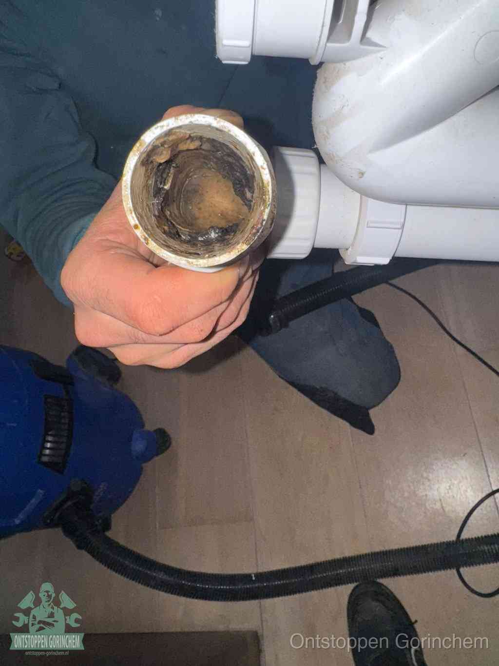 Een hand houdt een losgekoppeld PVC-afvoerbuisstuk vast dat van binnen volledig is dichtgeslibd met vet, vuil en aanslag, de meest voorkomende oorzaak van een verstopte afvoer in Gorinchem