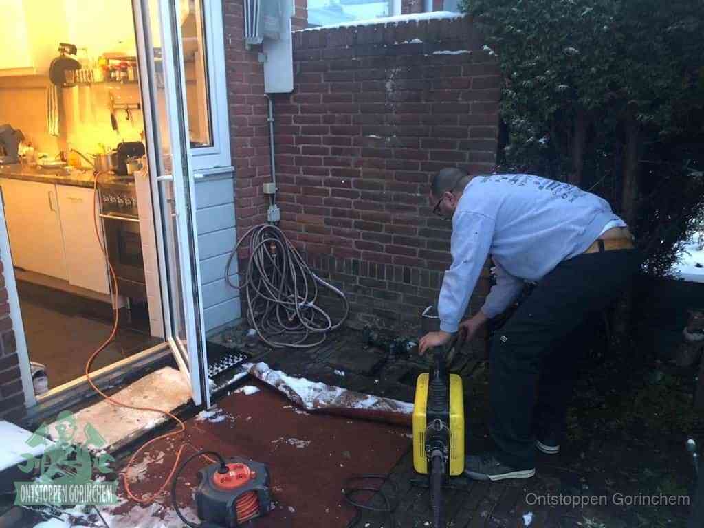 Een monteur werkt buiten bij een open riool-/grondput met een elektrische ontstoppingsmachine om een verborgen afvoerprobleem op te sporen in Gorinchem