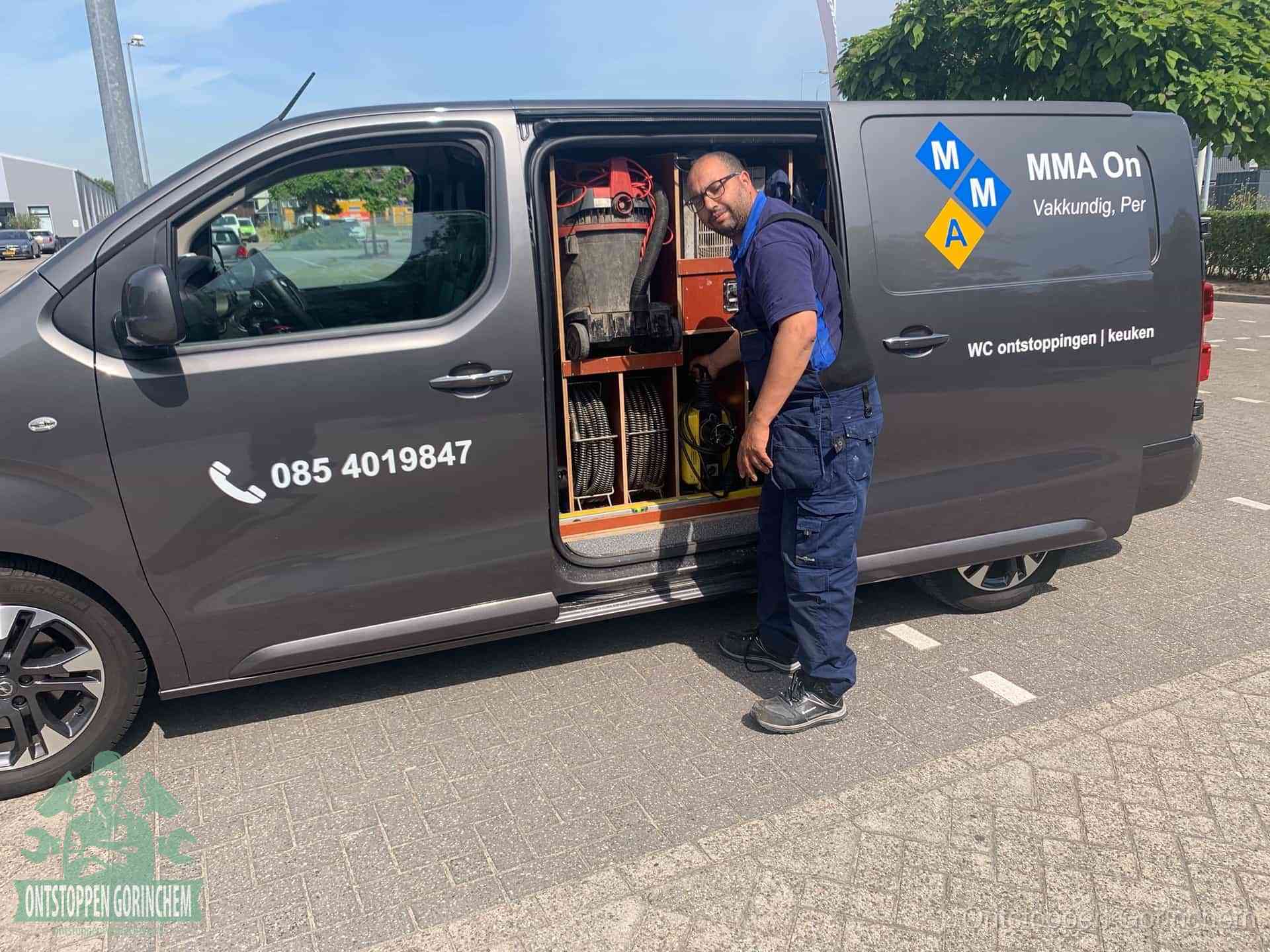 Een monteur bij de open schuifdeur van zijn bedrijfsbus op een parkeerplaats, klaar om de oorzaak van terugkerende afvoerverstoppingen aan te pakken in Gorinchem