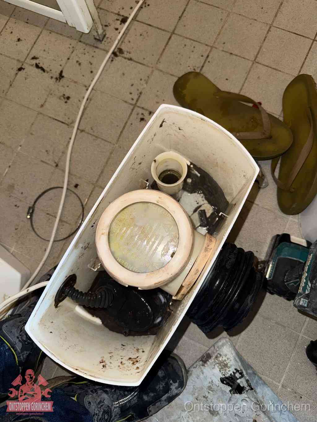 Een gedemonteerde toiletpot op de vloer met ontstoppingsveer en gereedschap ernaast, het verwijderen van een vastzittend voorwerp uit de wc in Gorinchem