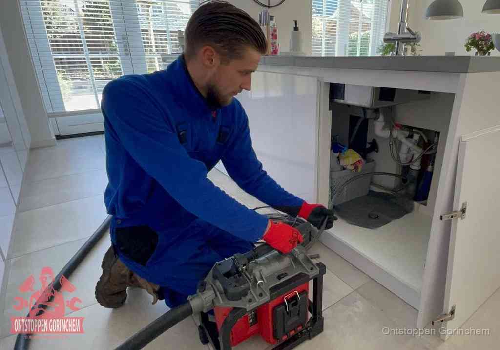 Een monteur voert een professionele elektrische ontstoppingsmachine in de afvoer onder de spoelbak tijdens het gootsteen ontstoppen in Gorinchem
