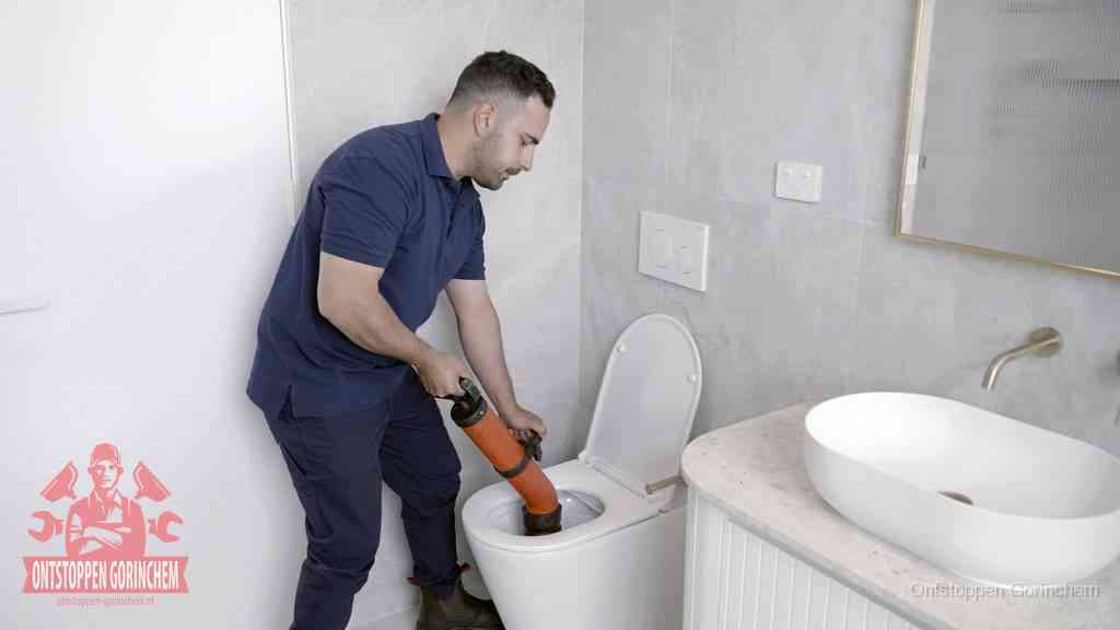 Een man gebruikt een handmatige luchtdruk-ontstopper in een modern betegeld toilet om zelf de wc te ontstoppen in Gorinchem